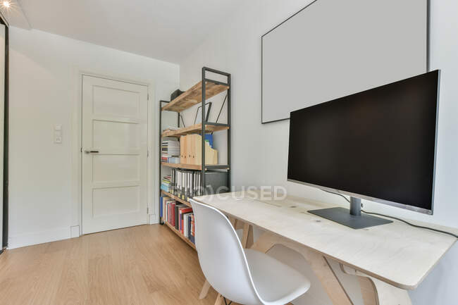 Stuhl am Schreibtisch mit modernem Computermonitor an der Wand mit Whiteboard im hellen Raum mit Büchern über Helme und Tür — Stockfoto