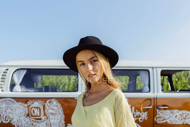 Cute blonde girl dressed in summer clothes with a hat standing outside a van — Stock Photo