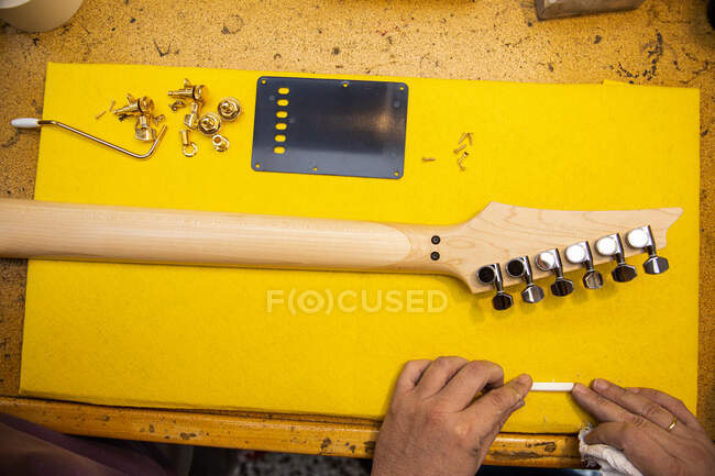 Vue du dessus du luthier masculin anonyme à la table avec cou de guitare électrique en bois avec touches de réglage en métal dans l'atelier — Photo de stock