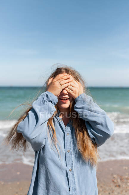 Young female covering face with hands while standing on coastline on sunny summer day — Stock Photo