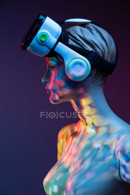 Manequim feminino com fone de ouvido VR em pé sob iluminação multicolorida brilhante contra fundo violeta — Fotografia de Stock