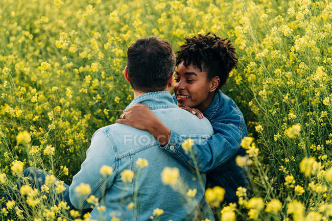 Liebendes junges multiethnisches Paar in lässiger Kleidung, das sich beim romantischen Date am sonnigen Tag in einer üppig blühenden Wiese anschaut — Stockfoto