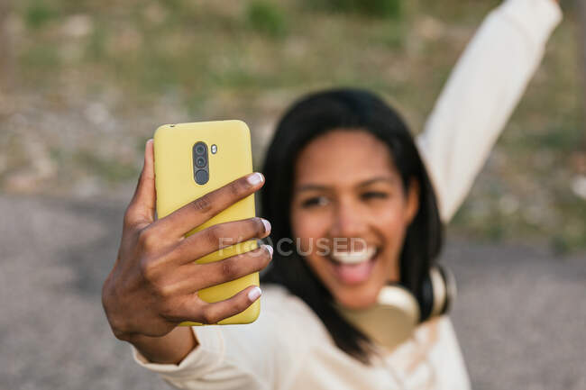 Щаслива етнічна жінка, що сидить на дошці, знімаючи власний портрет на мобільному телефоні — стокове фото