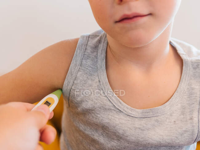 Coltiva genitore irriconoscibile con termometro elettronico che misura la temperatura del ragazzo malato anonimo che ha freddo — Foto stock