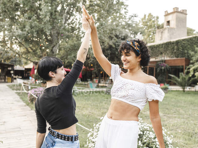 Friendly smiling diverse females giving high five to each other while standing in summer garden and having fun — Stock Photo