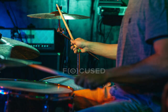 Zugeschnittener, bis zur Unkenntlichkeit konzentrierter männlicher Musiker, der in einem Club mit grüner und blauer Neonbeleuchtung Schlagzeug spielt — Stockfoto