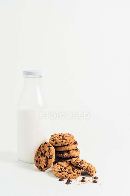 Куча сладкого хрустящего печенья с шоколадной крошкой на столе и молоком на белом фоне в номере — стоковое фото