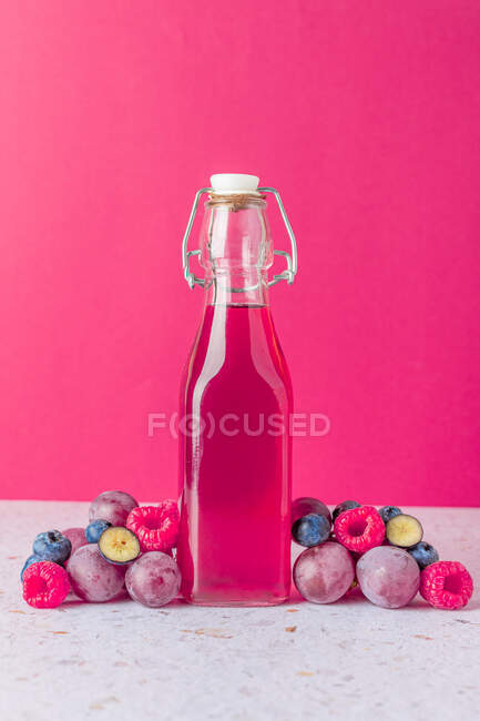 Glass bottle of fresh fruits juice surrounded with ripe berries served on table with glasses on pink background — Stock Photo