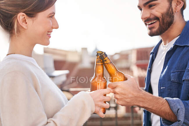 Entzückte junge Freunde in lässiger Kleidung klimpern mit Bierflaschen und chillen gemeinsam auf der Terrasse — Stockfoto