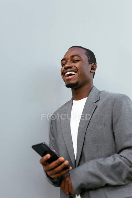 Sorrindo empresário afro-americano em uso formal navegando telefone celular e olhando para longe com o sorriso dos dentes — Fotografia de Stock