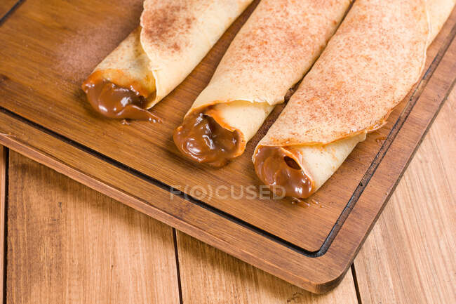 Сверху свежие вкусные блинчики со сладкой начинкой из лече, подаваемые на деревянной доске на кухне — стоковое фото