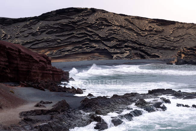 Vista panorámica del océano espumoso contra la playa de Ciclos y el volcán Guincho en Golfo Yaiza Lanzarote Islas Canarias España - foto de stock