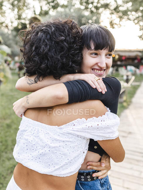 Позитивная любящая многонациональная пара гомосексуальных женщин обнимается, стоя на дорожке в летнем парке — стоковое фото