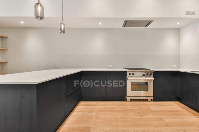 Современная хромированная печь на просторной кухне с минималистской черной мебелью и перчатками в светлой квартире — стоковое фото