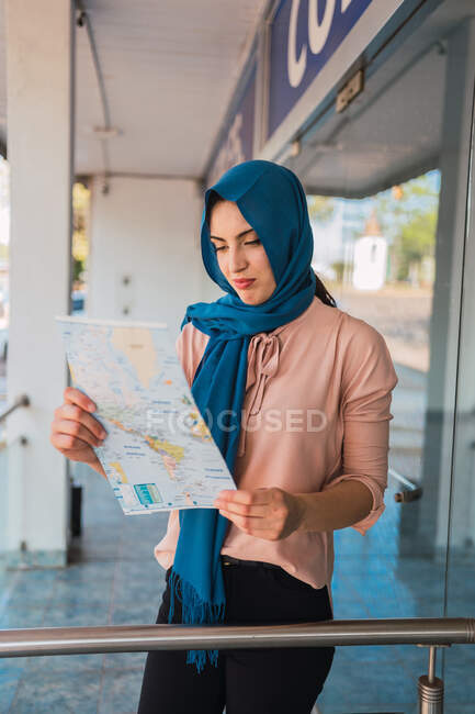 Focada turista muçulmana no tradicional hijab de pé na rua e navegando com mapa de papel na cidade — Fotografia de Stock