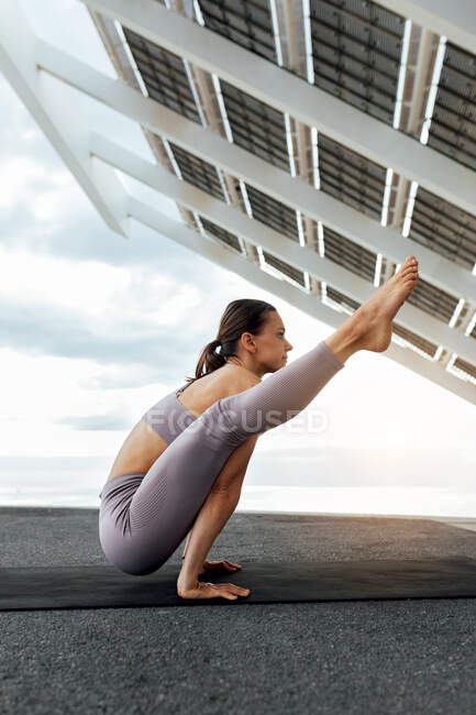 Ganzkörper-Seitenansicht einer starken Sportlerin bei Tittibhasana-Haltung auf Matte während eines intensiven Yoga-Trainings in der Nähe von Solarzellen in Barcelona — Stockfoto