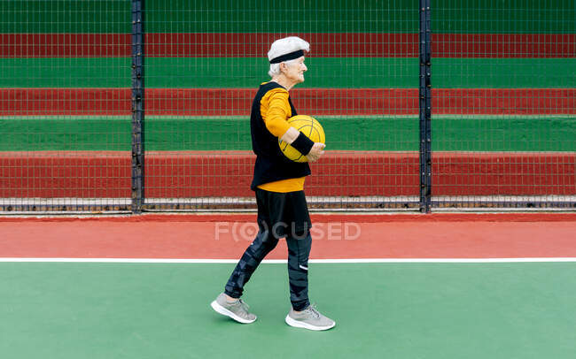 Боковой вид зрелой женщины в спортивной одежде и повязке, смотрящей в сторону во время игры в баскетбол — стоковое фото