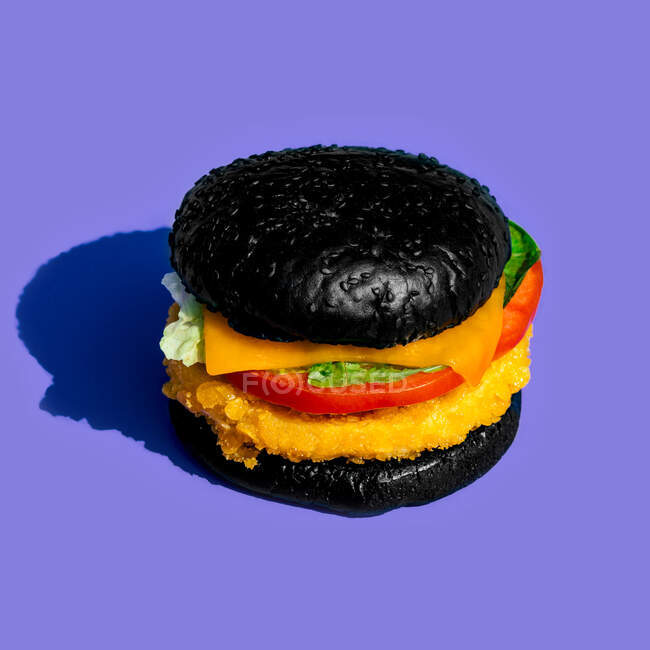 Du dessus burger frais avec pain noir et légumes sur fond lilas — Photo de stock