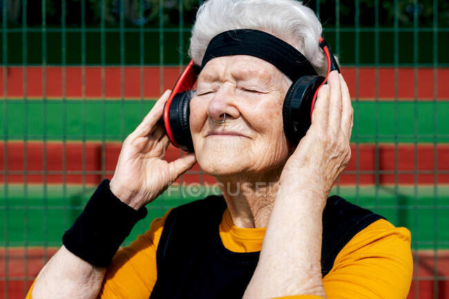 Contenu femelle mature avec nez percé dans l'usure active écouter des chansons dans les écouteurs tout en se tenant terrain de sport près du filet — Photo de stock