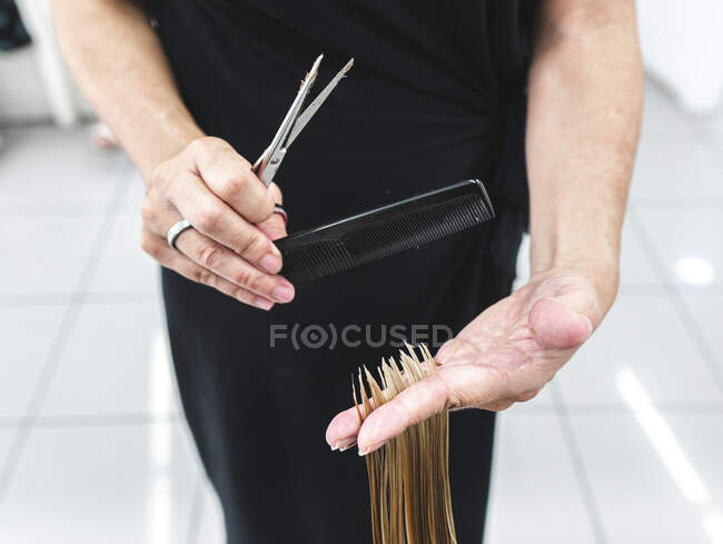 Crop unrecognizable hairdresser using scissors to cut fair hair of client in beauty salon — Stock Photo