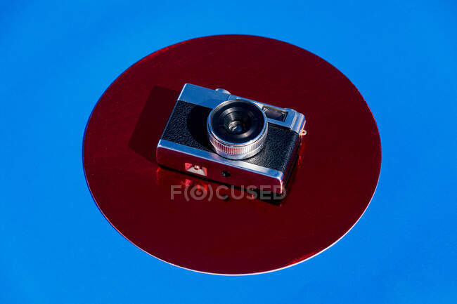 From above retro photo camera placed on metallic red circle on blue background — Stock Photo