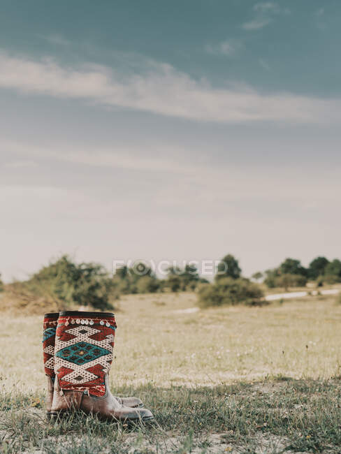 Пара хиппи сапоги с творческими украшениями и красочные геометрические узоры помещены на травянистых лугах в сельской местности в летний день — стоковое фото