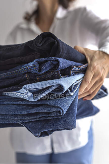 Cortar fêmea anônima em camisa branca com pilha de jeans azuis nas mãos — Fotografia de Stock