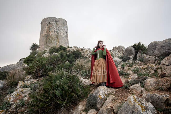 Full body side view of female in Victorian styled clothes standing on cliff with moss near sea in misty weather — Stock Photo