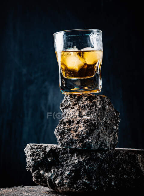 Whiskey with ice cubes served in crystal glass placed on rough surface against black background — Stock Photo