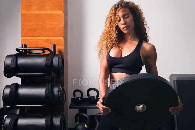 Konzentrierte Muskelsportlerin steht tagsüber mit schwerer Hantelscheibe beim Training im Fitnessstudio — Stockfoto