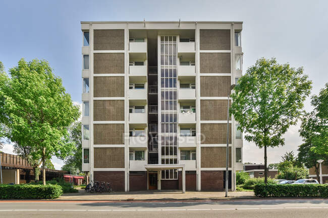 Diseño creativo de mampostería exterior edificio de varios pisos con balcones entre árboles cubiertos bajo el cielo claro en Amsterdam Holanda Septentrional - foto de stock