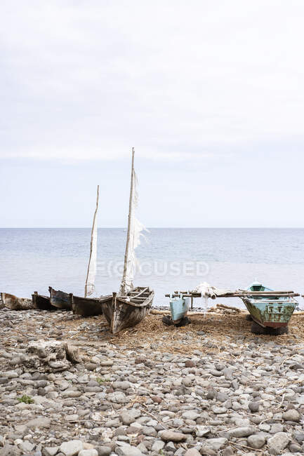 Old wooden boats moored on rocky coast near calm ocean n So Tom and Prncipe under cloudy sky in daylight — Stock Photo