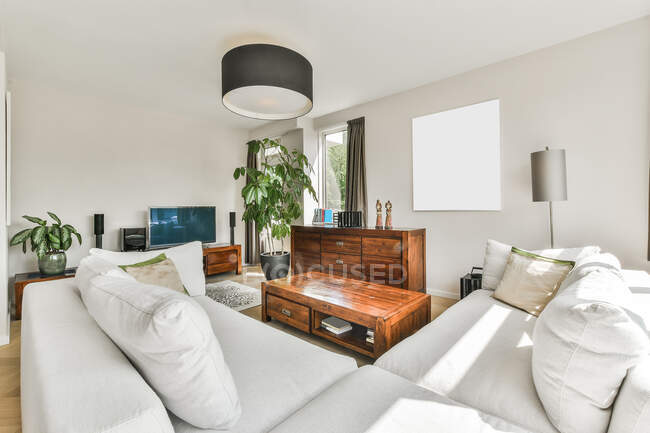 Interior da sala de estar contemporânea com mesa de madeira entre sofá e commode contra painel na parede em casa — Fotografia de Stock