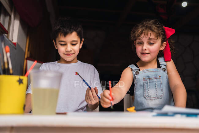 Positive kids with paintbrushes painting with colorful watercolors on paper at table — Stock Photo