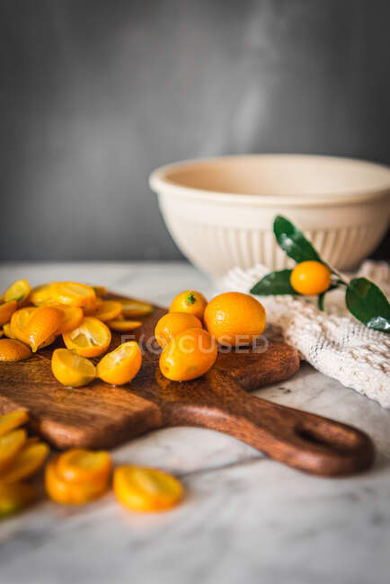 Montón de kumquats de corte naranja fresco sobre tabla de cortar de madera colocada sobre mesa de mármol con toalla en la cocina - foto de stock