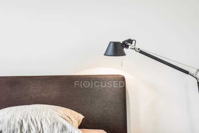 Черная лямка с перламутровым светом на белом фоне над удобной кроватью с подушкой в светлой спальне стильной квартиры — стоковое фото