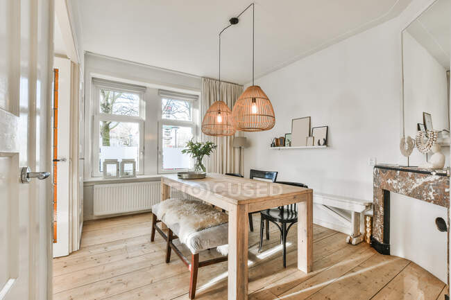 Design creativo della sala da pranzo con panca e tavolo in legno sotto le lampade appese contro la finestra in casa — Foto stock