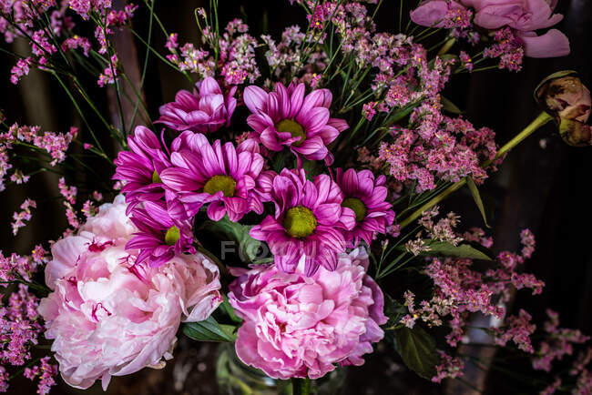 Bouquet of fresh colorful peonies and chrysanthemums in glass vase placed on weathered wooden chair near curtains in light room — Stock Photo