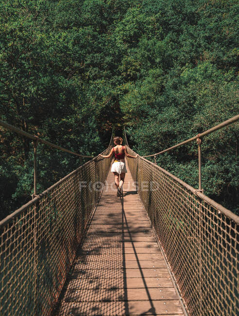 Rückansicht einer anonymen Forscherin, die an einem sonnigen Tag in Spanien auf einer Metallhängebrücke im Naturpark Fragas do Eume steht — Stockfoto