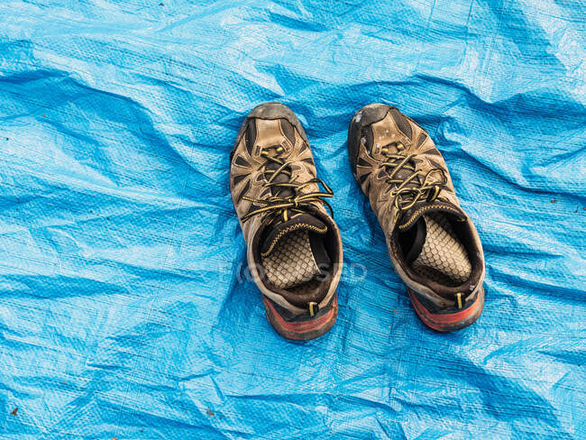 Desde arriba de los viejos zapatos de trekking de mala calidad colocados en la tienda de campaña azul en el día soleado - foto de stock