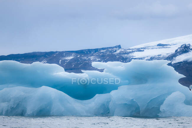 Paesaggio mozzafiato di un grande ghiacciaio galleggiante nel lago Jokulsarlon increspato circondato da montagne innevate contro il cielo coperto in Islanda — Foto stock