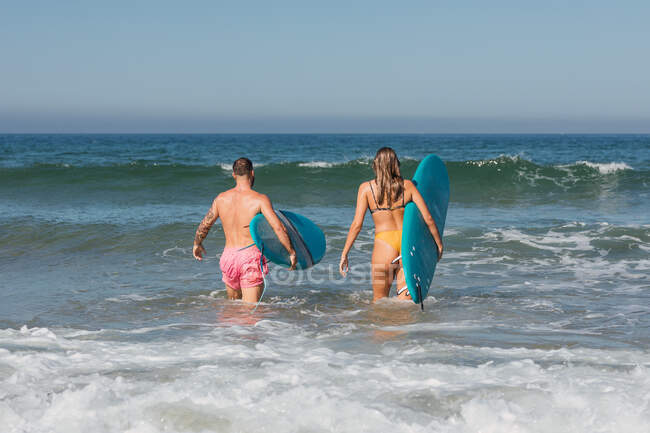 Visão traseira de corpo inteiro do casal esportivo em trajes de banho com pranchas de surf preparando-se para surfar em mar ondulado durante o treinamento do oceano iônico — Fotografia de Stock