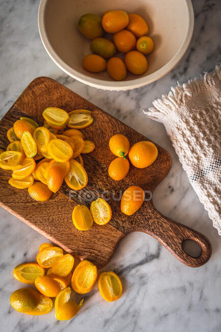 Haufen frische orange geschnittene Kumquats auf hölzernem Schneidebrett auf Marmortisch mit Handtuch in der Küche — Stockfoto