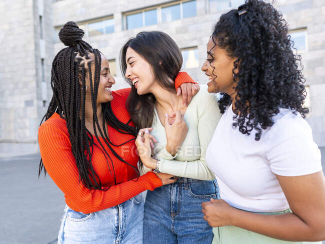 Cheerful multiracial women standing and laughing while spending time together on city street in daylight — Stock Photo