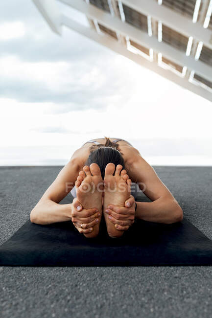 Mulher descalça flexível irreconhecível praticando postura Paschimottanasana no mar durante o treinamento de ioga perto do painel solar na rua na cidade de Barcelona — Fotografia de Stock