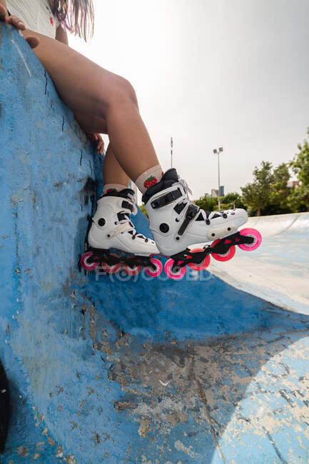 Crop anonymous female legs in white roller blades with pink wheels resting on concrete pavement in skate park — Stock Photo