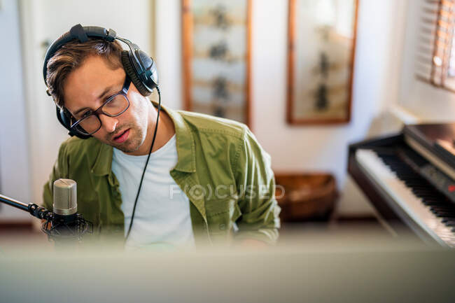 Зверху концентрований хлопець з навушниками сидить за столом і працює на комп'ютері — стокове фото