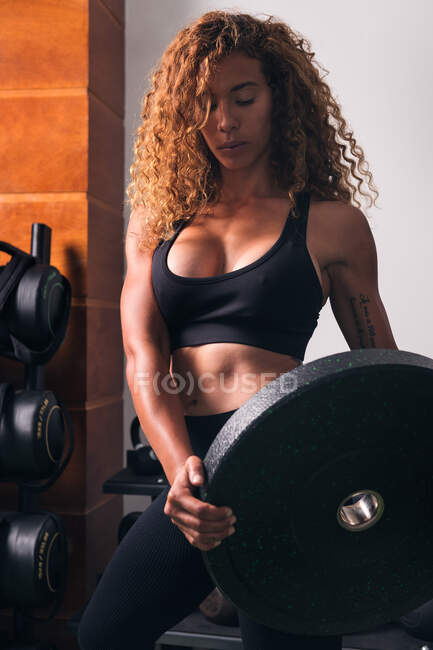 Концентрована м'язова спортсменка стоїть з важкою вагою тарілки під час тренувань у спортзалі вдень — стокове фото