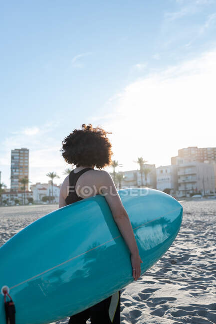 Обратный вид на неузнаваемую серфингистку в гидрокостюме с доской для сёрфинга, стоящую на берегу моря, умытую морем — стоковое фото
