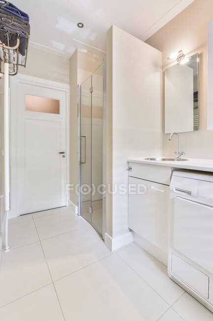 Cupboards with sink and washing machine located near shower cabin and door in light contemporary bathroom — Stock Photo